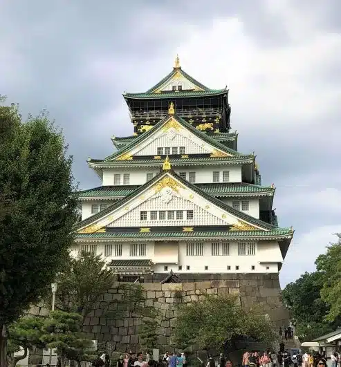 Osaka Castle in Osaka, Japan. White castle with gold decorations. People waling under the castle.